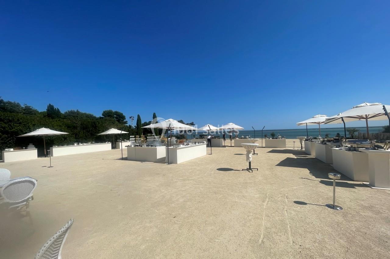 Terrasse en plein air avec parasols blancs, mobilier clair et vue sur la mer sous un ciel bleu dégagé.