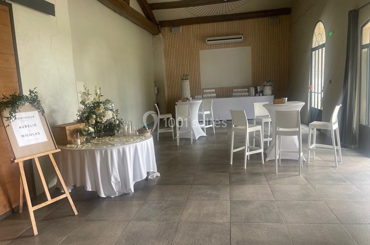 Salle de réception lumineuse avec tables décorées, panneau de bienvenue et espace bar en arrière-plan.