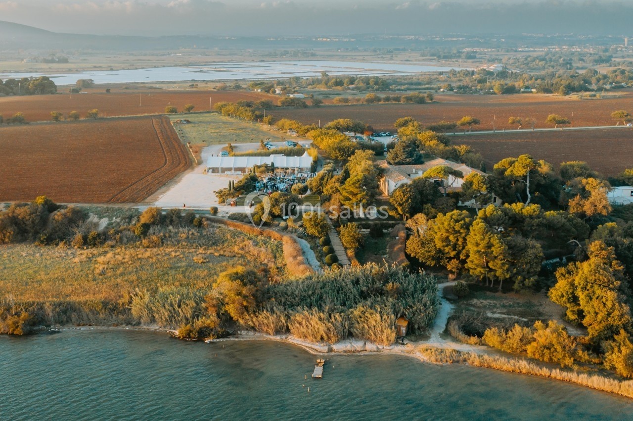 Vue aérienne d'un domaine entouré de champs, de végétation et bordé par un plan d'eau avec un petit ponton.