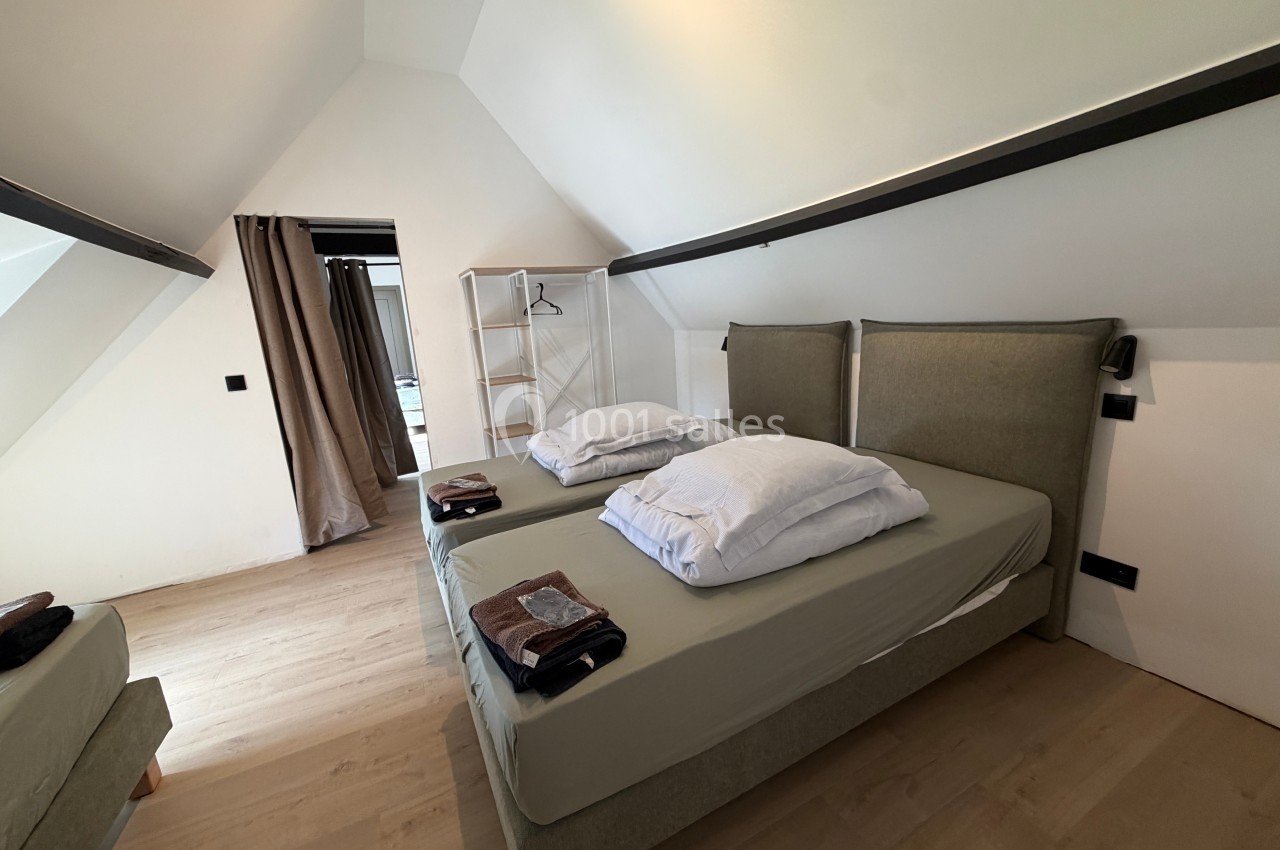 Chambre mansardée avec deux lits simples, linge plié, parquet clair et penderie ouverte en arrière-plan.