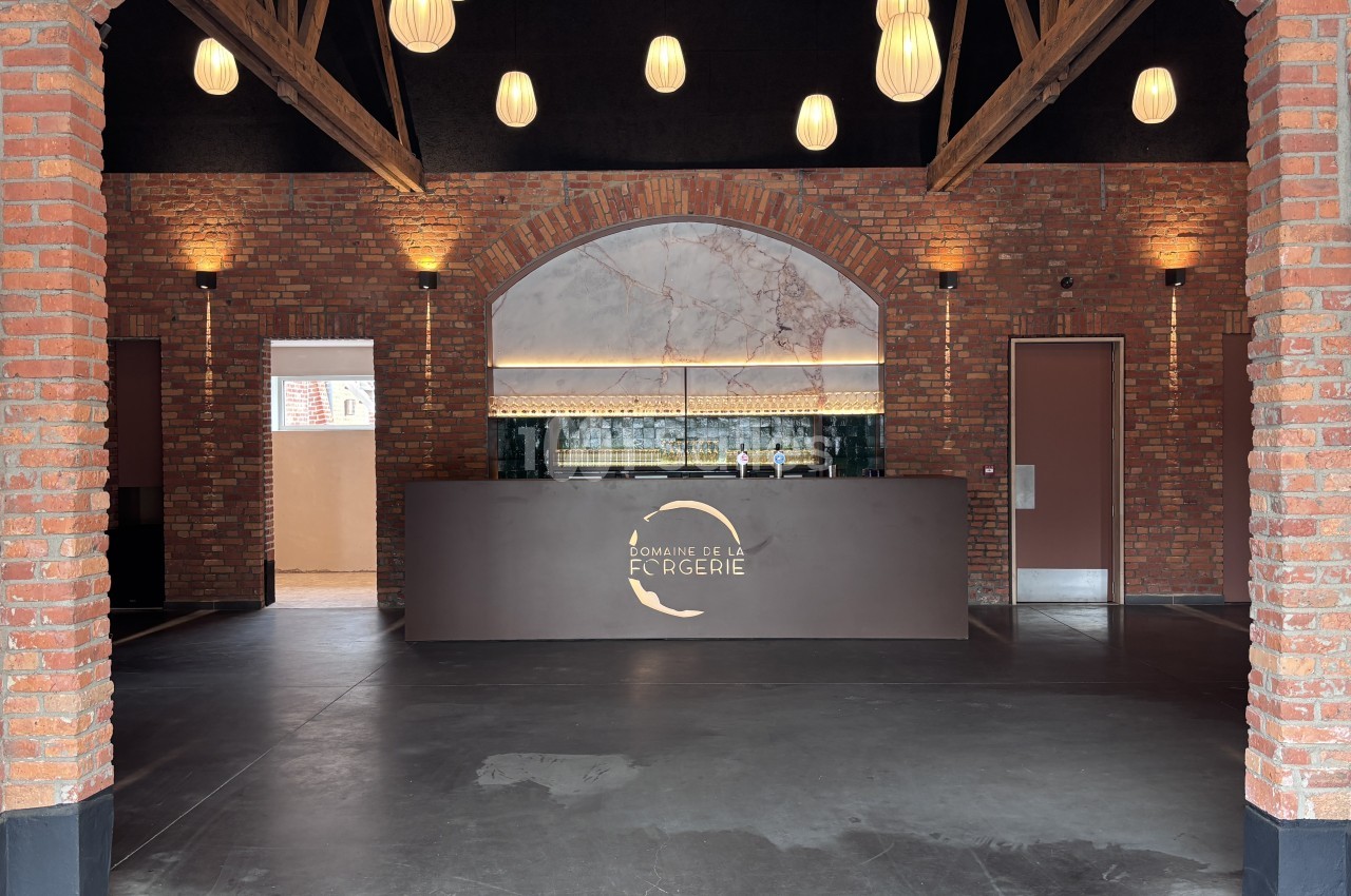 Salle vide aux murs de brique apparente, avec poutres en bois, suspensions et un comptoir de bar sous une arche.