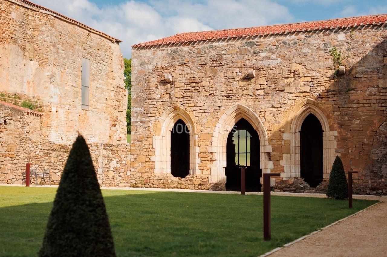 Ruines d'un bâtiment en pierre avec des arches gothiques, entourées d'une pelouse et de buis taillés.