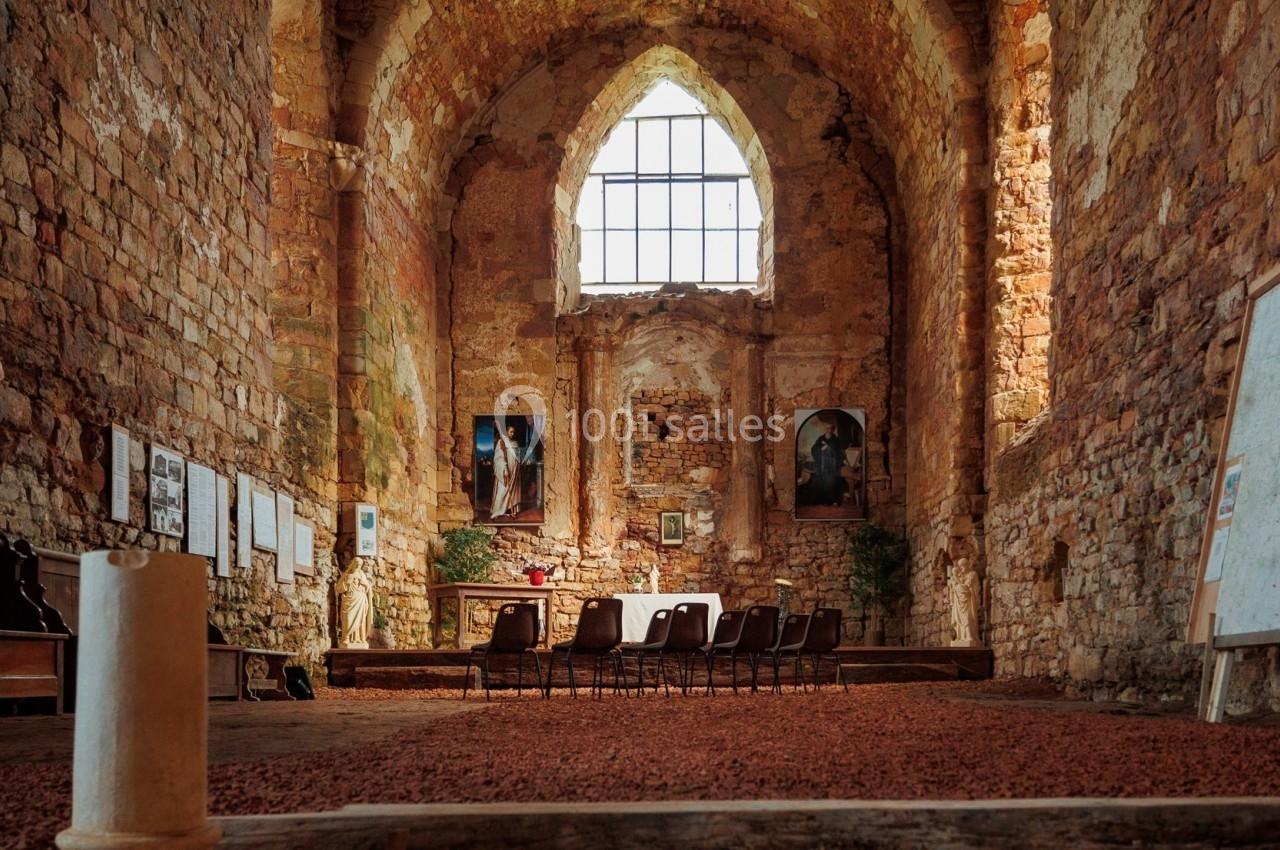 Intérieur d'une église en pierre ancienne avec des chaises alignées, un autel et une grande fenêtre gothique.