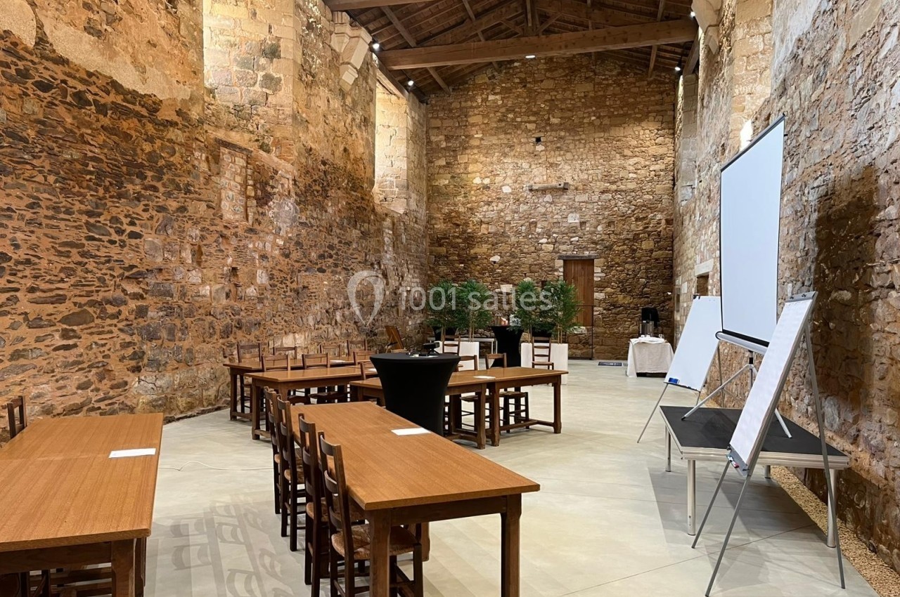 Salle en pierre avec tables, chaises, tableaux de présentation et plantes, aménagée pour une réunion ou un événement.