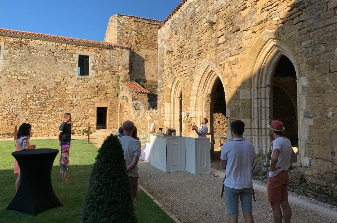 Personnes rassemblées dans la cour d'un bâtiment historique en pierre, près d'un comptoir blanc, par temps ensoleillé.