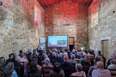 Salle en pierre avec tables hautes noires, boissons, plantes décoratives et chaises disposées pour un événement.