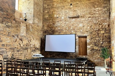 Salle en pierre avec tables hautes noires, boissons, plantes décoratives et chaises disposées pour un événement.