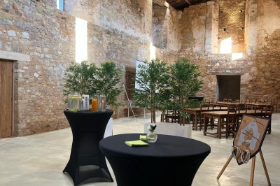 Salle en pierre avec tables hautes noires, boissons, plantes décoratives et chaises disposées pour un événement.