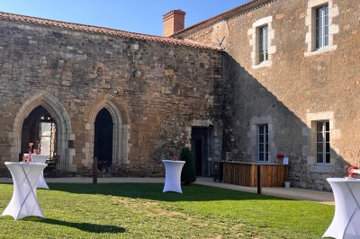 Miniature Location salle Bournezeau (Vendée) - Abbaye de Trizay #59 Cour intérieure d'un bâtiment historique en pierre, aménagée avec des tables hautes et éclairée par un soleil éclatant.