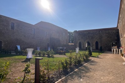 Miniature Location salle Bournezeau (Vendée) - Abbaye de Trizay #62 Cour intérieure d'un bâtiment historique en pierre, aménagée avec des tables hautes et éclairée par un soleil éclatant.