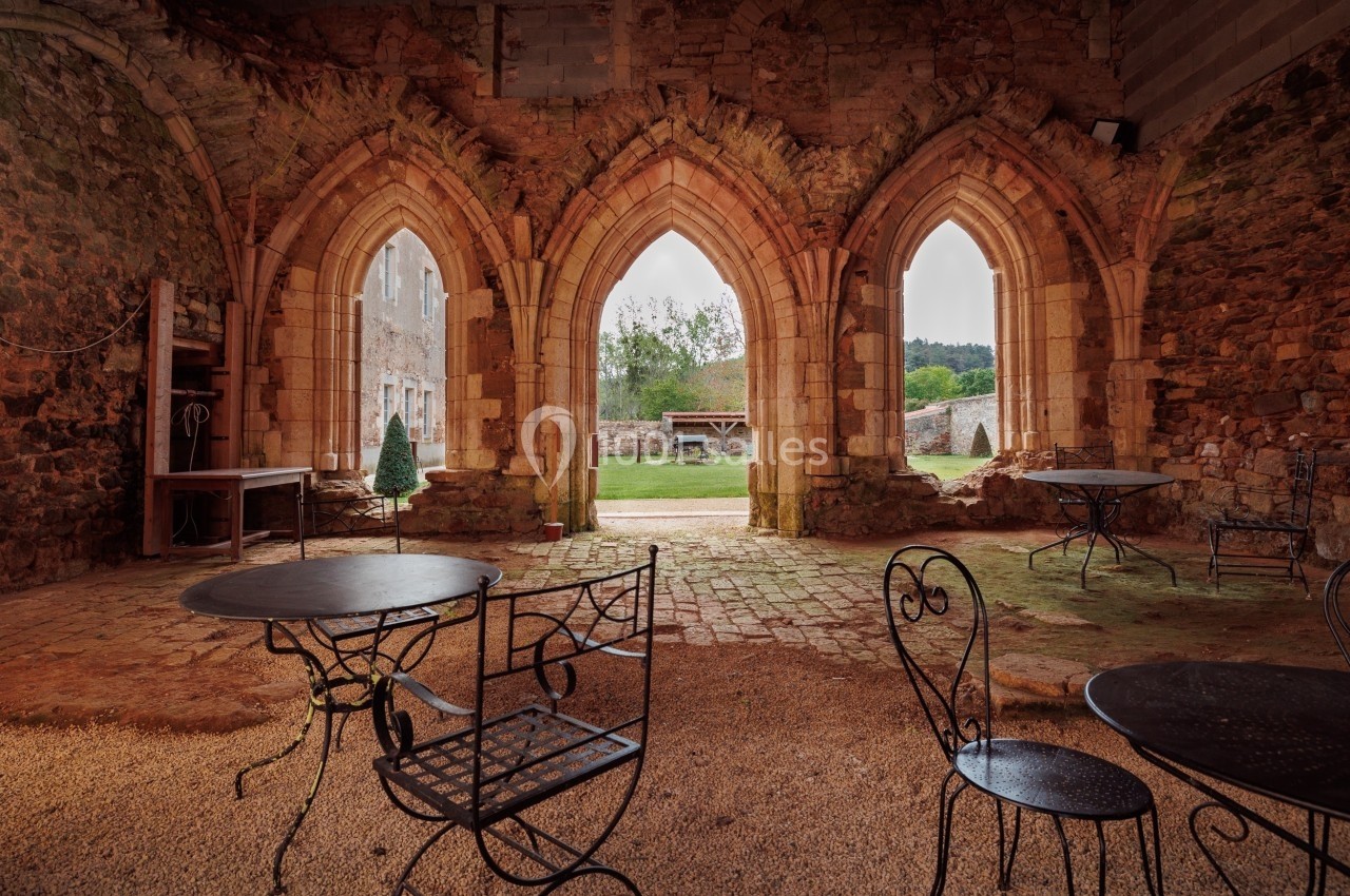 Vue intérieure d'une ancienne bâtisse en pierre avec arches ouvertes donnant sur une cour verdoyante.