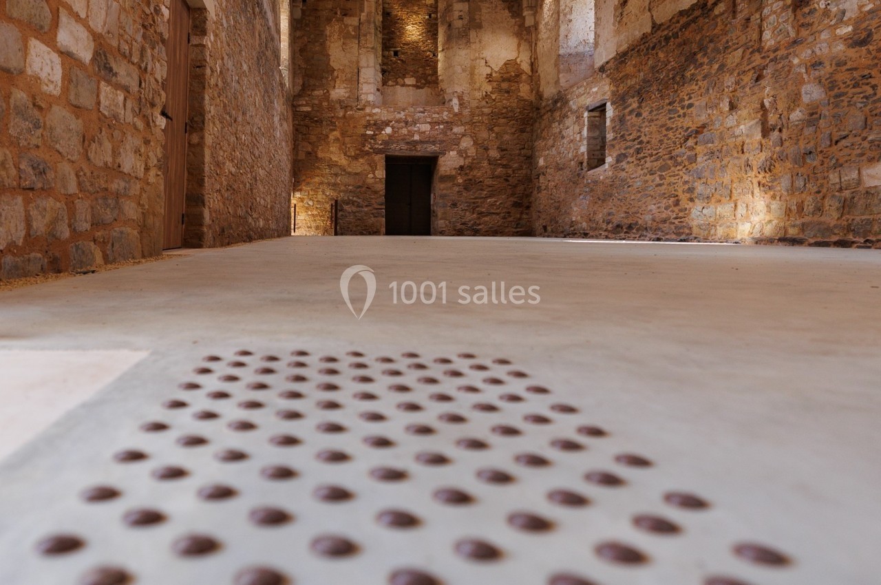 Intérieur d'un bâtiment en pierre avec un sol tactile en relief et un plafond en bois apparent.
