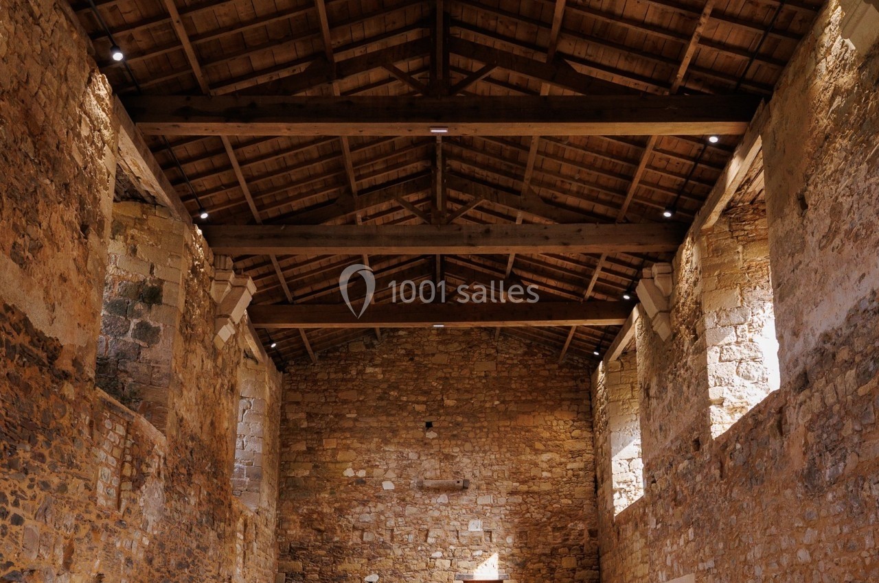 Intérieur d'un bâtiment en pierre avec un toit en bois, éclairé par la lumière naturelle entrant par une porte ouverte.