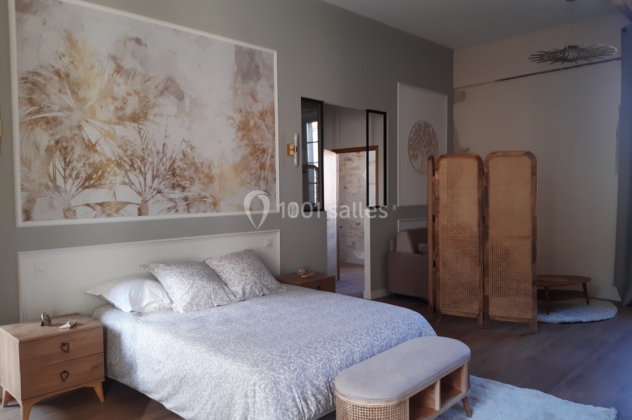 Chambre lumineuse avec lit double, paravent en bois, mobilier en rotin et décoration murale végétale.