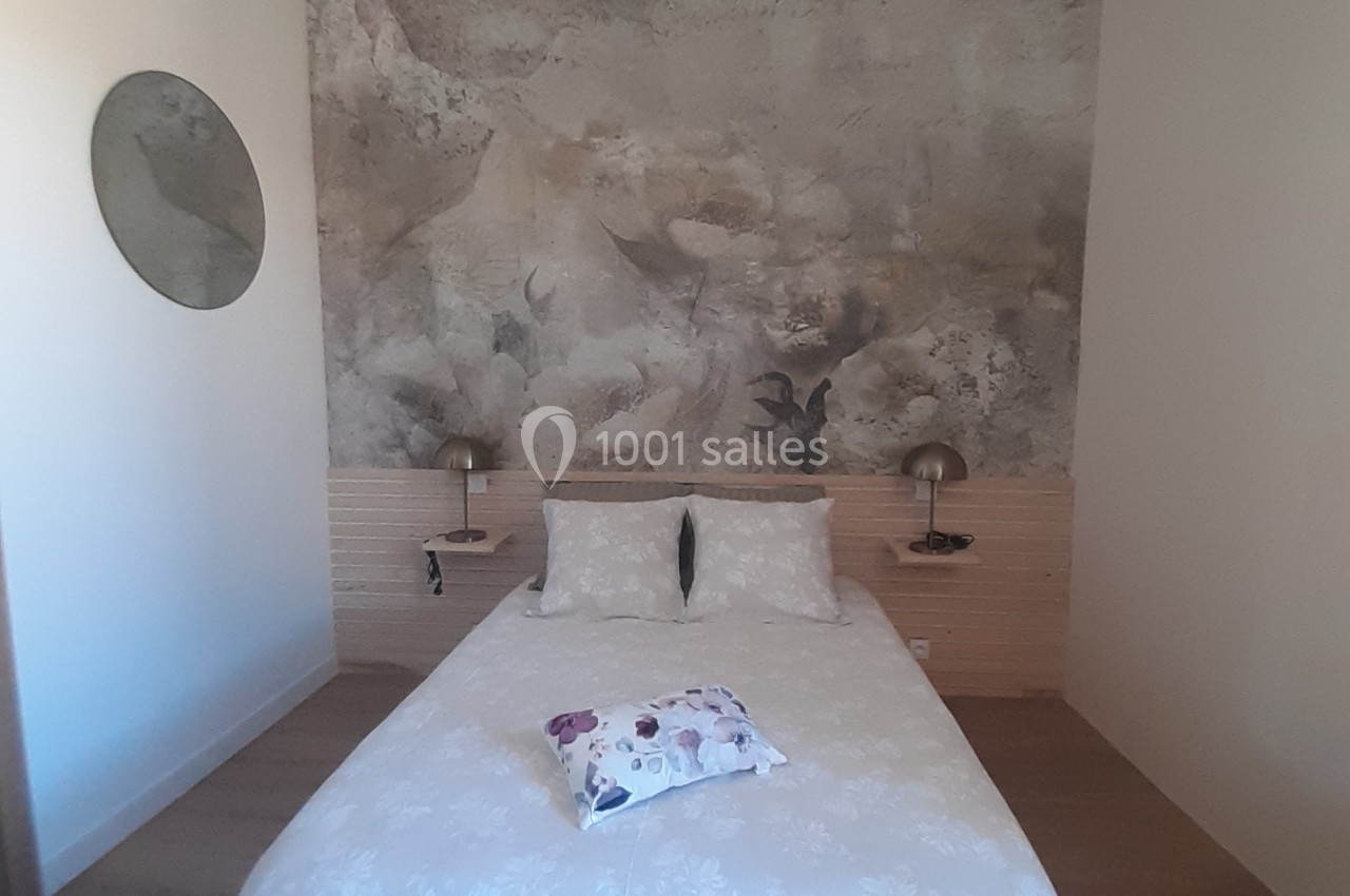 Chambre avec un lit double, mur décoré d'une fresque florale, lampes murales et miroir rond sur le côté.