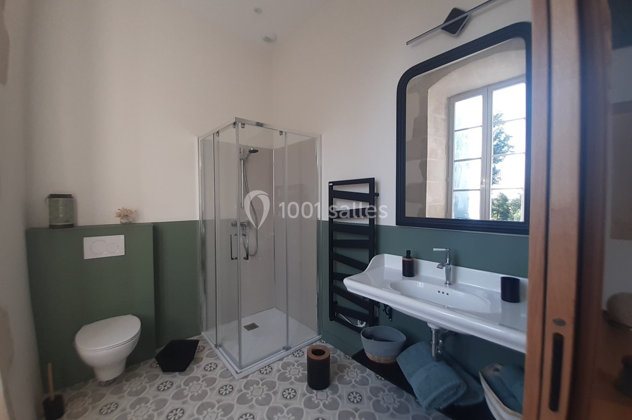 Salle de bain lumineuse avec douche vitrée, lavabo double, toilettes suspendues et sol en carreaux à motifs.