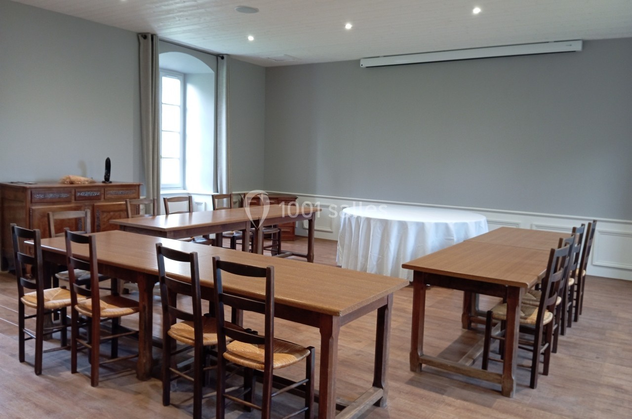 Salle de réunion avec tables en bois disposées en U, chaises en paille et une table ronde drapée de blanc.