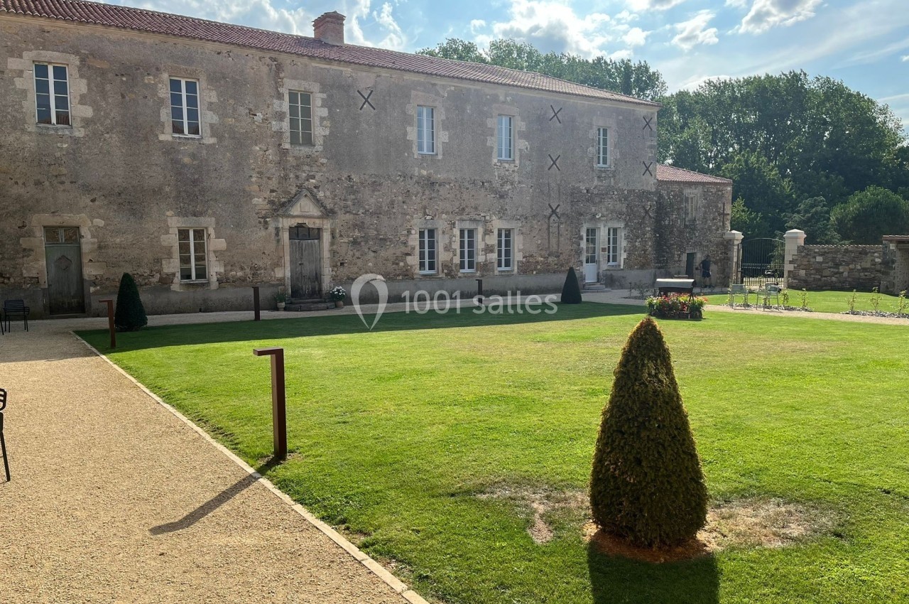 Bâtiment en pierre ancienne entouré d'une pelouse bien entretenue, sous un ciel partiellement nuageux.