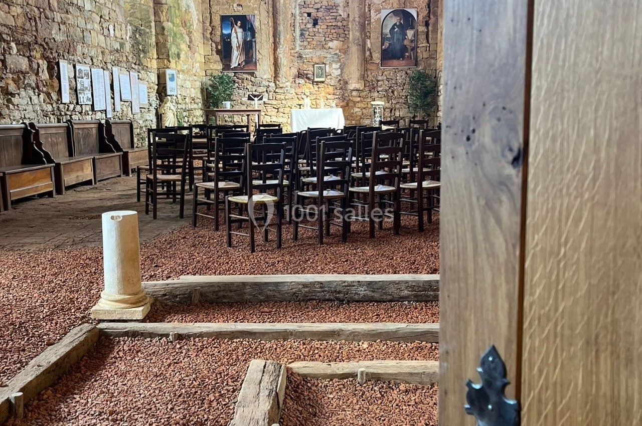 Vue intérieure d'une chapelle en pierre avec des rangées de chaises, un autel éclairé par une grande fenêtre.