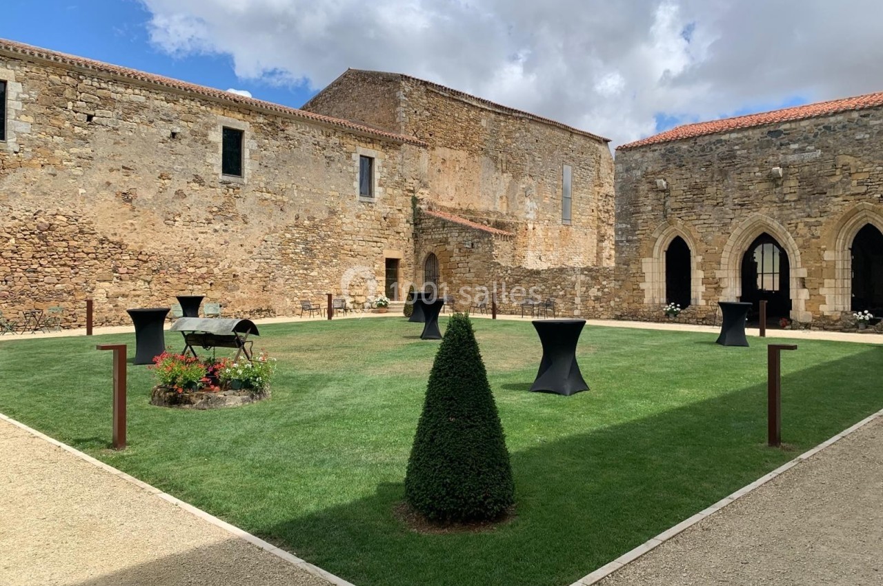 Cour intérieure d'un bâtiment historique en pierre, avec pelouse, arbustes taillés et tables hautes noires.