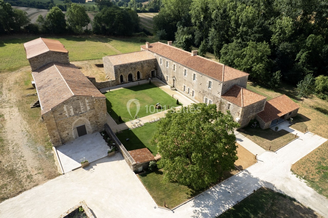 Vue aérienne d'un domaine rural avec bâtiments en pierre, toits en tuiles, cour centrale et espaces verts environnants.