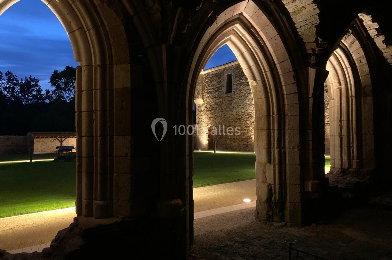 Vue nocturne d'arches en pierre éclairées, donnant sur une cour avec pelouse et murs en pierre illuminés.