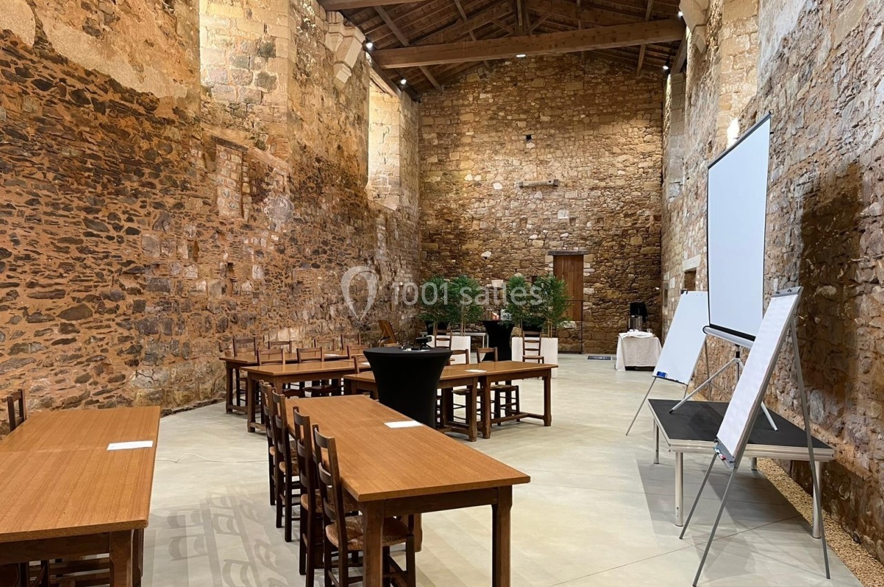 Salle en pierre avec tables, chaises, tableaux de présentation et plantes, aménagée pour une réunion ou un événement.