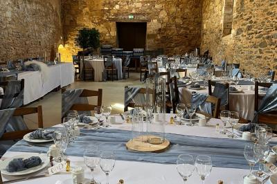 Table dressée avec nappes blanches, verres et seaux à glace, dans une salle en pierre avec de grandes fenêtres.