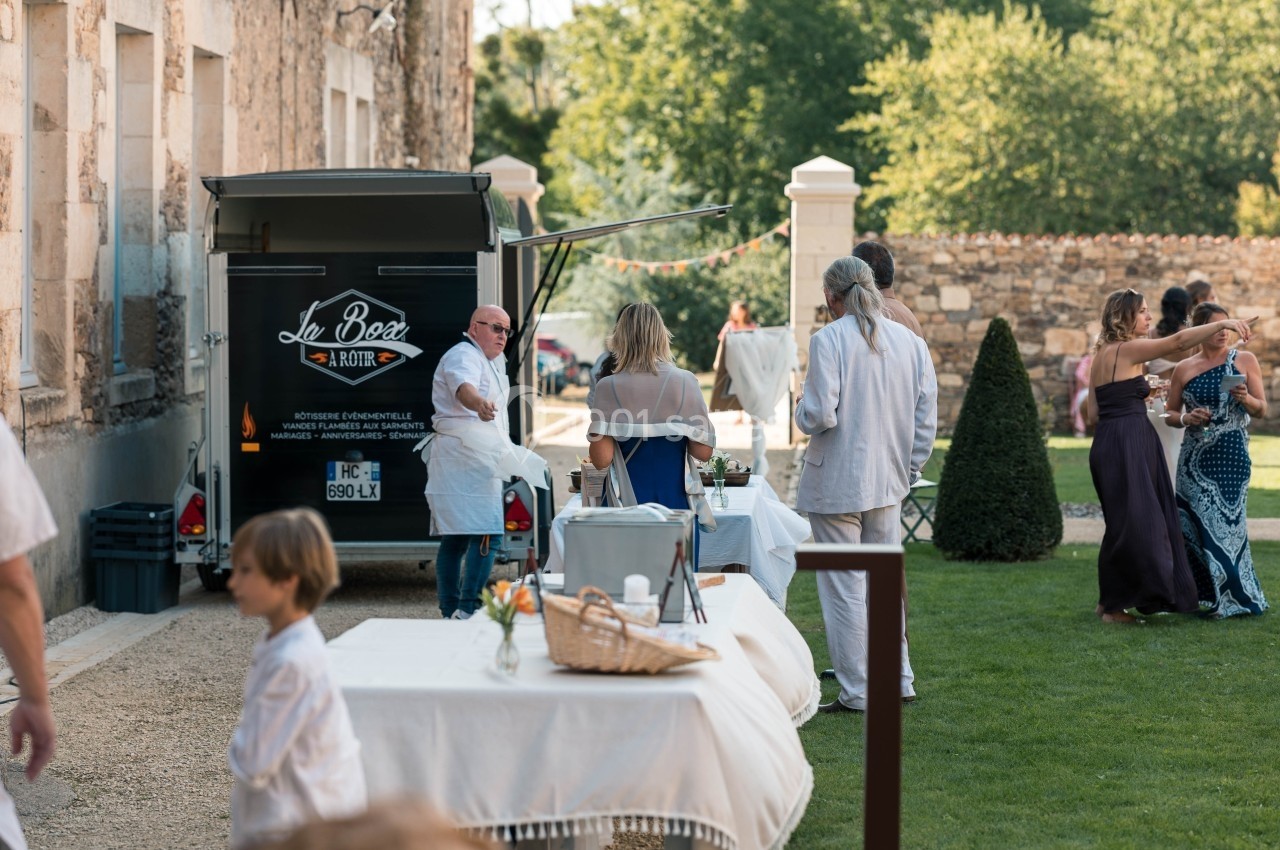 Un food truck stationné près d'une bâtisse en pierre sert des invités lors d'un événement en plein air.