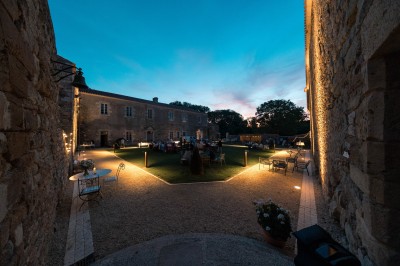 Table dressée avec nappes blanches, verres et seaux à glace, dans une salle en pierre avec de grandes fenêtres.
