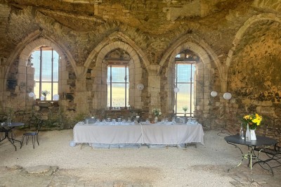 Table dressée avec nappes blanches, verres et seaux à glace, dans une salle en pierre avec de grandes fenêtres.
