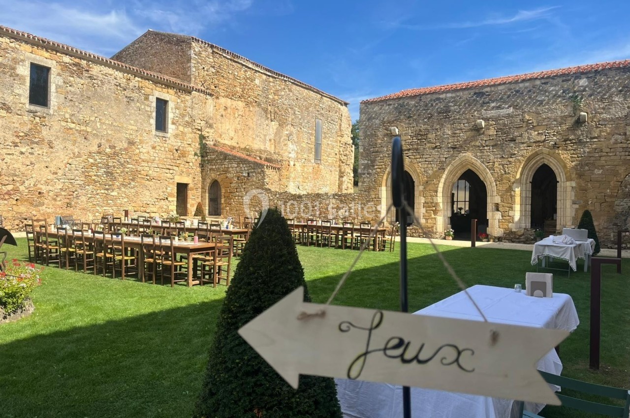 Cour intérieure d'un bâtiment en pierre avec des tables et chaises disposées pour un événement, panneau ’Jeux’ au premier…