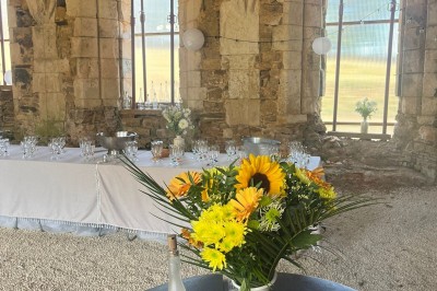 Table dressée avec nappes blanches, verres et seaux à glace, dans une salle en pierre avec de grandes fenêtres.