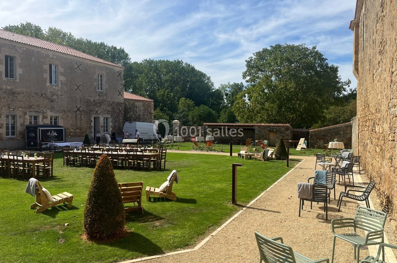Cour extérieure avec pelouse, chaises, tables et bâtiments en pierre sous un ciel dégagé.