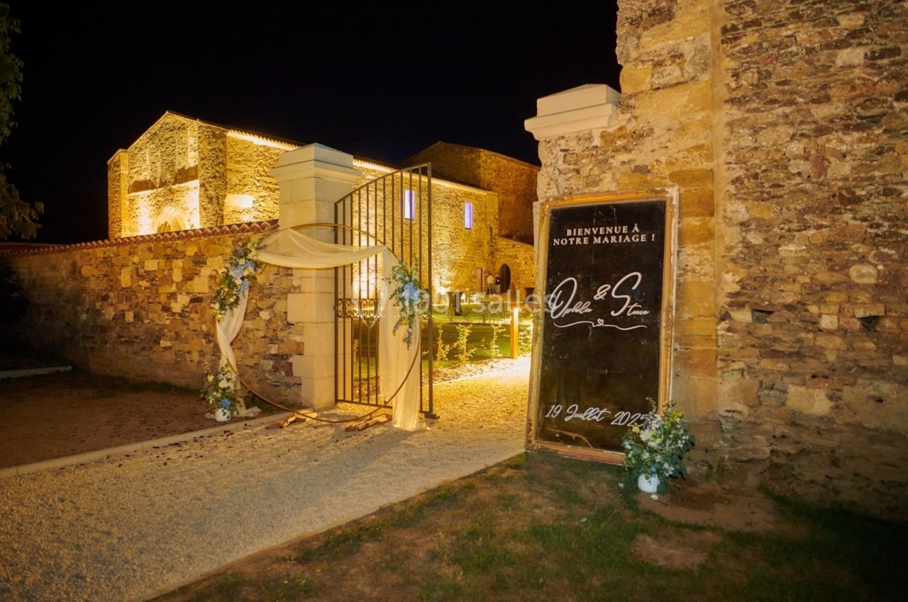 Entrée illuminée d'une bâtisse en pierre avec une arche décorée et un panneau de bienvenue pour un mariage.