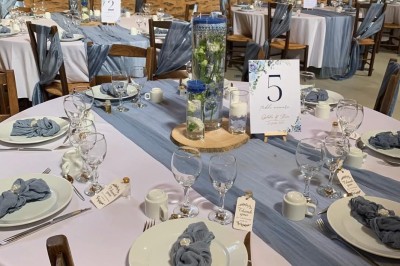 Table dressée avec nappes blanches, verres et seaux à glace, dans une salle en pierre avec de grandes fenêtres.
