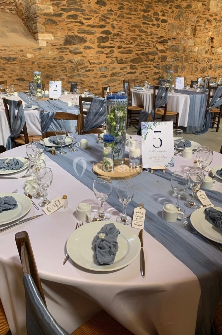 Tables élégamment dressées avec nappes blanches, chemins de table bleus, serviettes assorties et décorations florales.