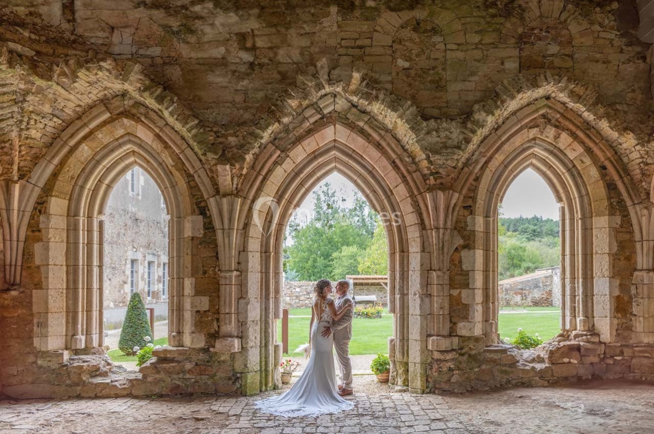 Un couple en tenue de mariage pose sous des arches en pierre dans un cadre historique et verdoyant.