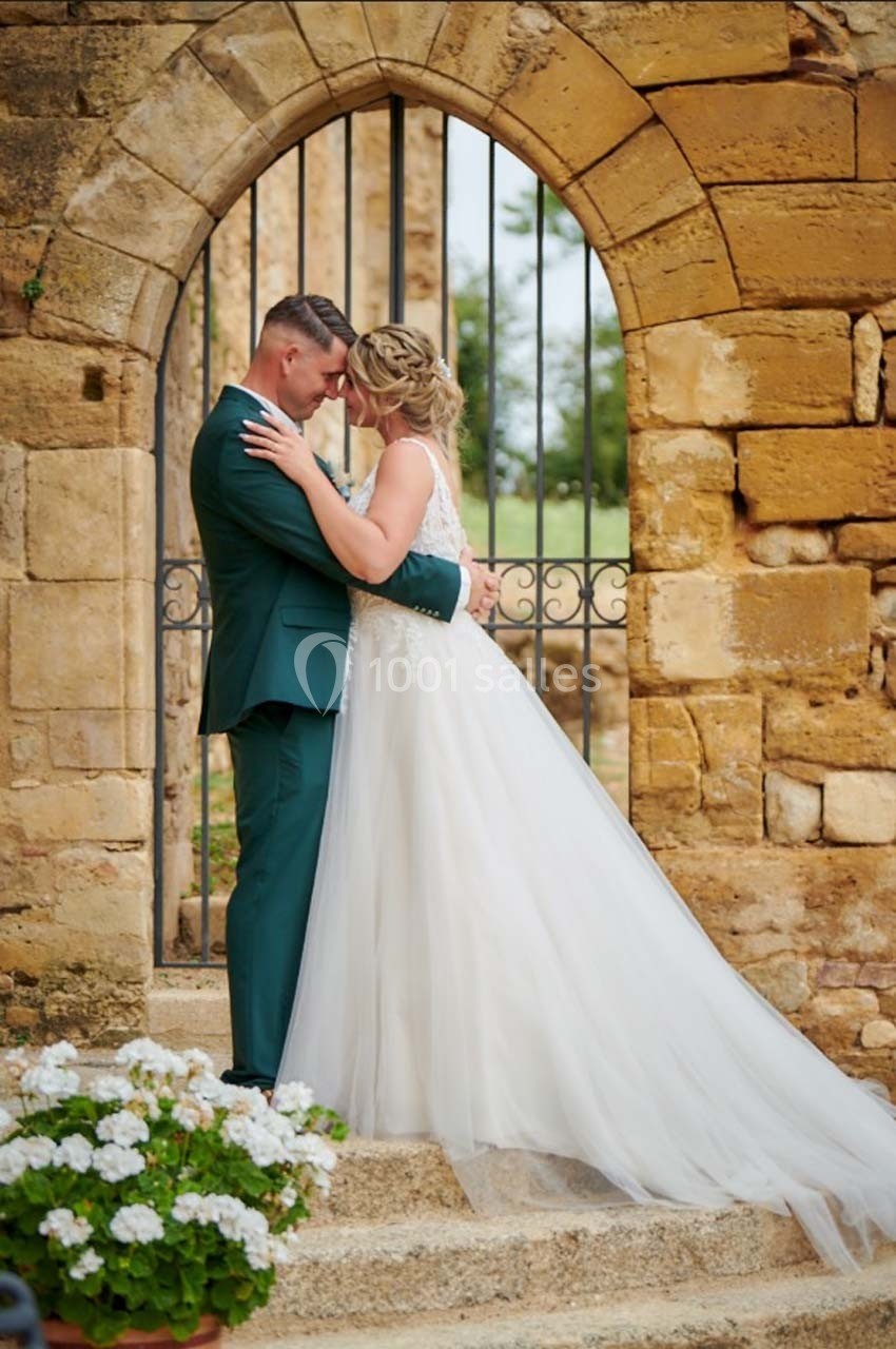 Un couple en tenue de mariage s'enlace devant une arche en pierre dans un cadre extérieur.