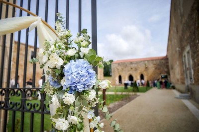 Table dressée avec nappes blanches, verres et seaux à glace, dans une salle en pierre avec de grandes fenêtres.