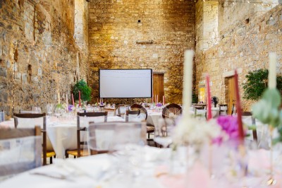 Cour intérieure d'un bâtiment historique en pierre, aménagée avec des tables hautes et éclairée par un soleil éclatant.