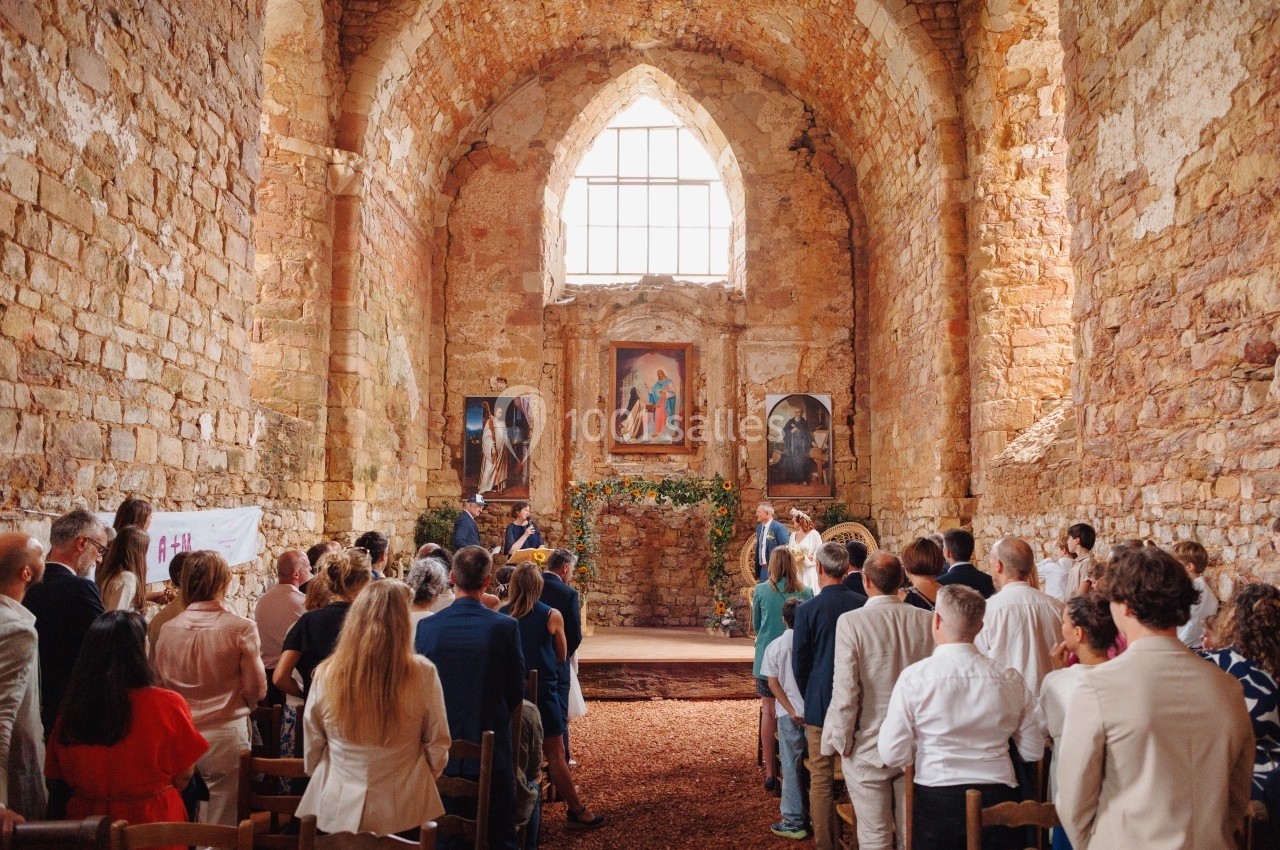 Cérémonie dans une église en pierre ancienne, avec des invités assis et debout face à l'autel décoré.
