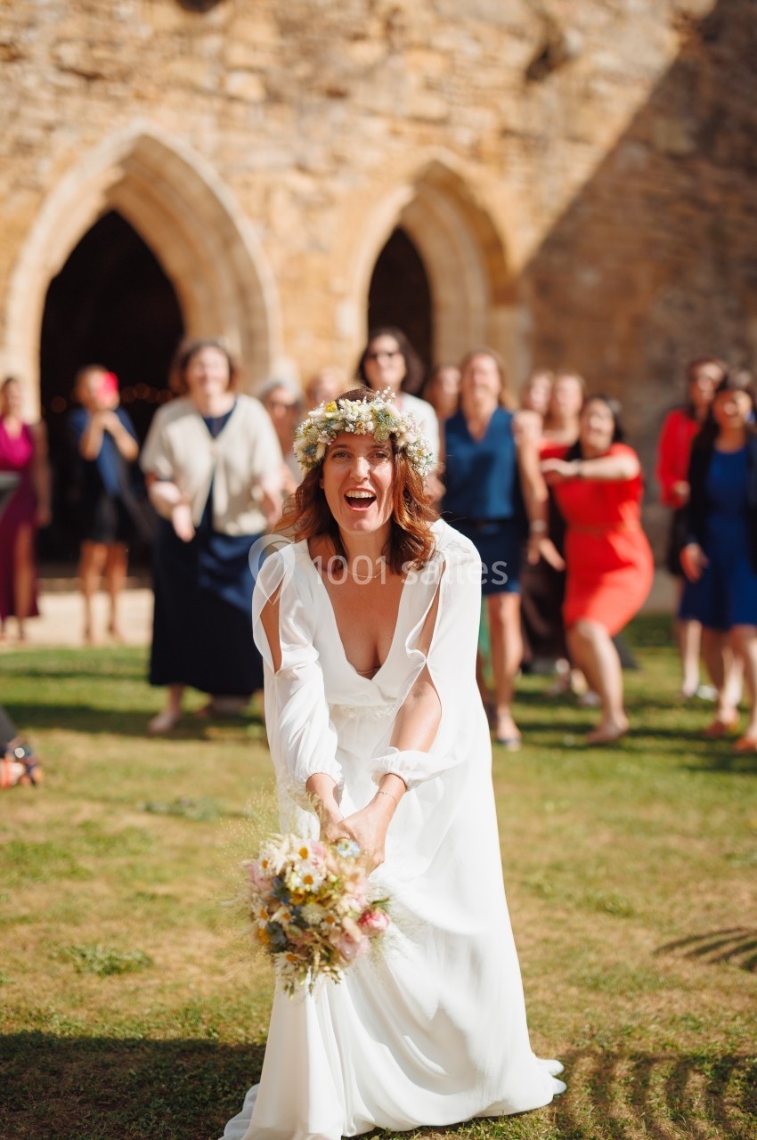 Une mariée souriante lance son bouquet de fleurs devant un groupe d'invités en extérieur près d'une église.