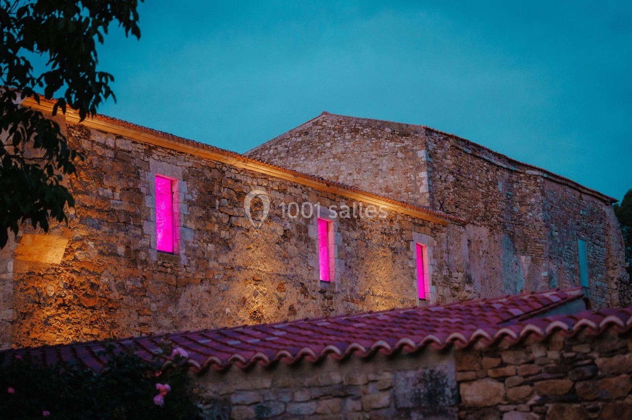 Façade en pierre d'un bâtiment ancien éclairée par des lumières roses sous un ciel crépusculaire.