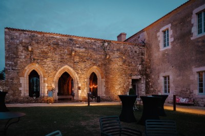 Cour intérieure d'un bâtiment historique en pierre, aménagée avec des tables hautes et éclairée par un soleil éclatant.