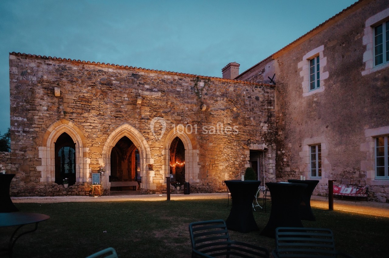 Façade en pierre d'un bâtiment historique éclairé de nuit, avec des arches gothiques et des tables en extérieur.