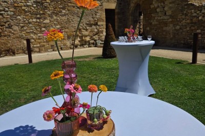 Cour intérieure d'un bâtiment historique en pierre, aménagée avec des tables hautes et éclairée par un soleil éclatant.