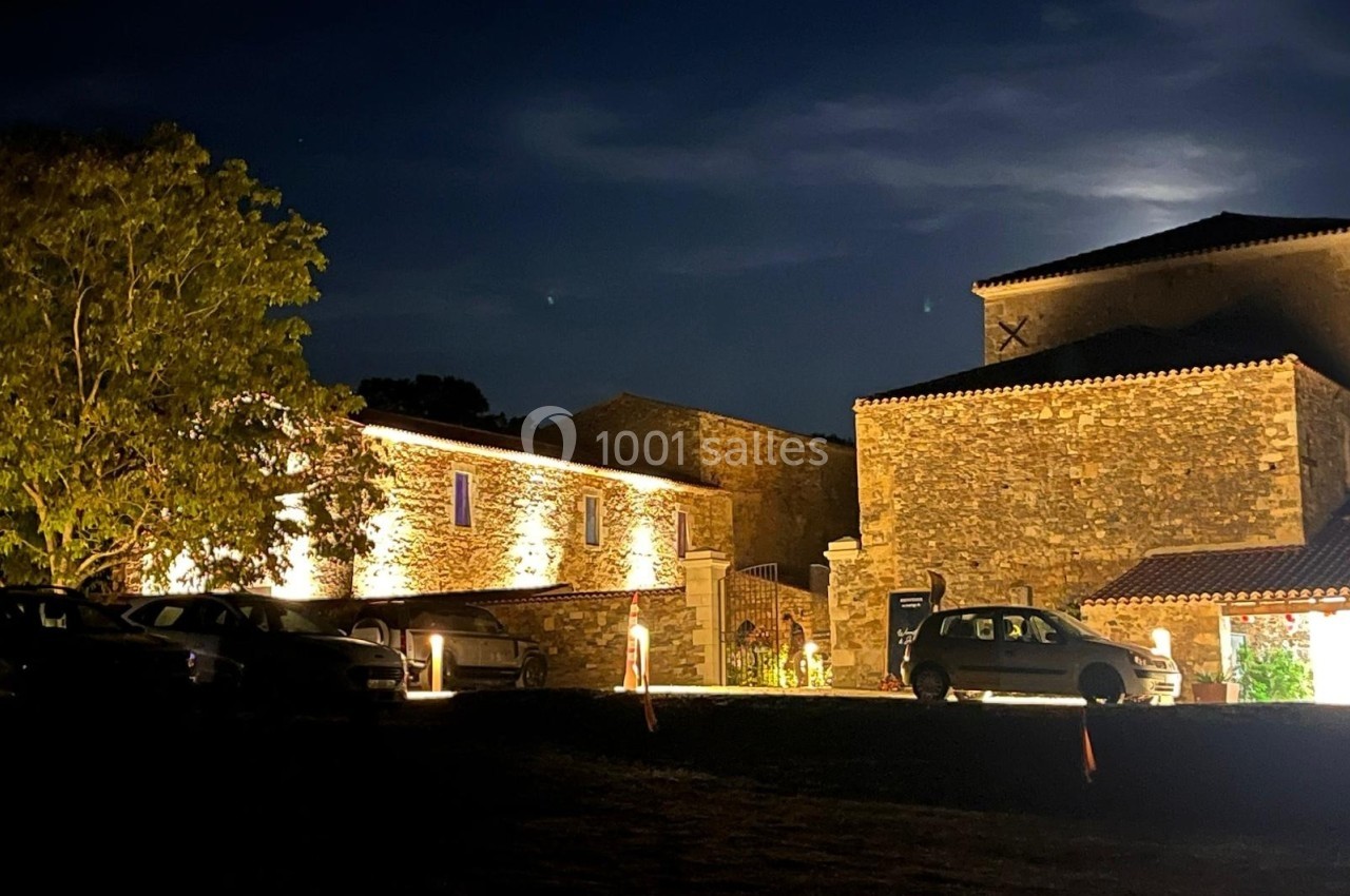Bâtiments en pierre éclairés la nuit, avec des voitures garées devant et un ciel sombre en arrière-plan.