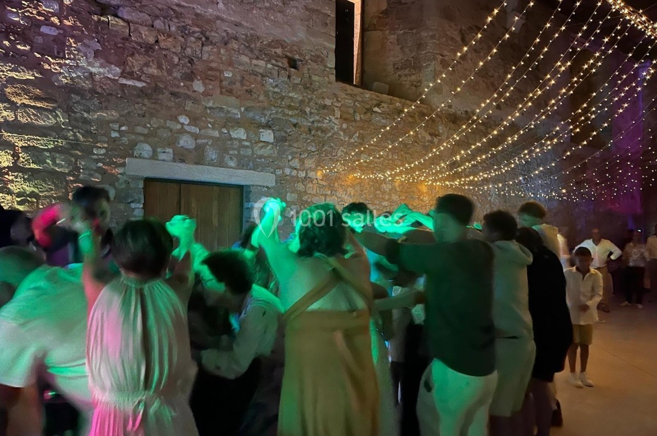 Des personnes dansent sous des guirlandes lumineuses dans une ambiance festive, près d'un mur en pierre.