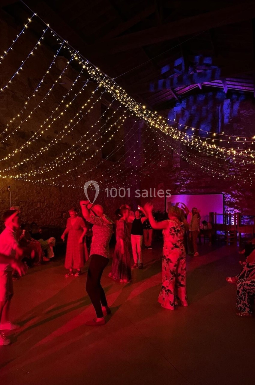 Personnes dansant sous des guirlandes lumineuses suspendues dans une salle en pierre avec éclairage rouge et violet.